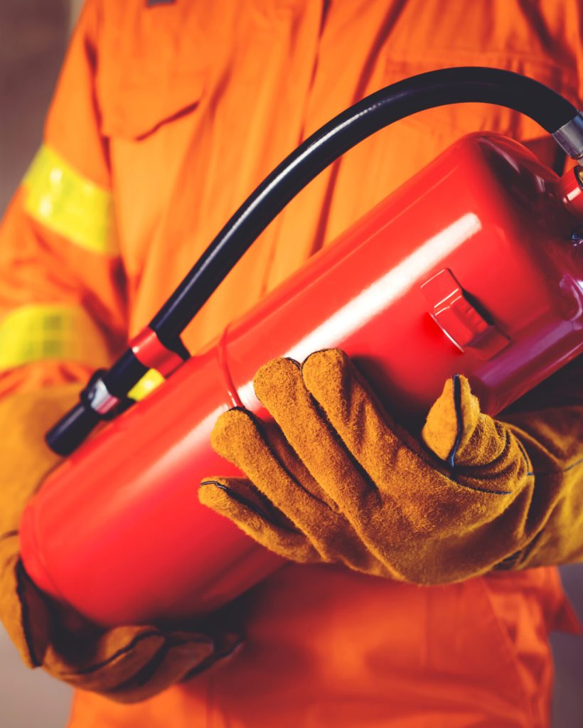 Fireman hand holding fire extinguisher. available in emergencies conflagration damage background. Safety concept.